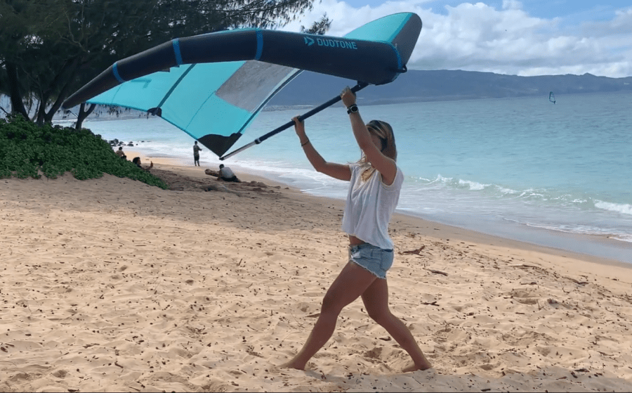 mujer en la arena de la playa con un wingfoil